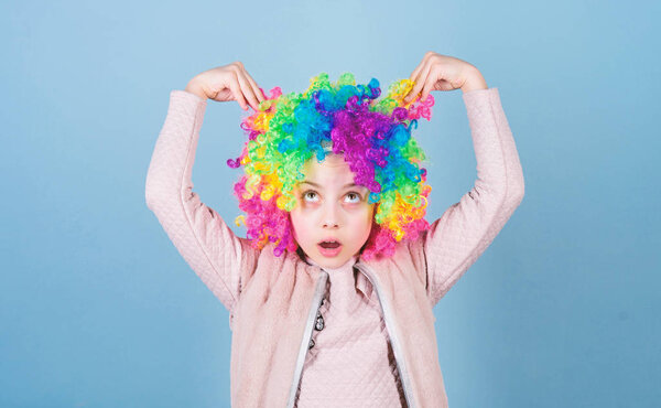 Playing with her hair. Funny kid with curly synthetic hair. Cute little girl with fancy hair. Adorable small child wearing bright clown hair wig