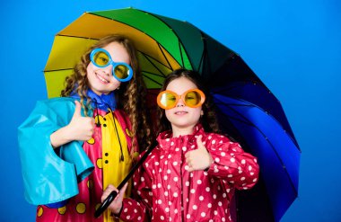 Uygun giysiler ile yağmurlu hava. Şemsiyenin altında yürü. Çocuklar kızlar şemsiye altında mutlu arkadaşlar. Parlak şemsiye. Mutlu çocukluk. Birlikte mutlu olmak daha kolay. Birileri bulut gökkuşağı olun