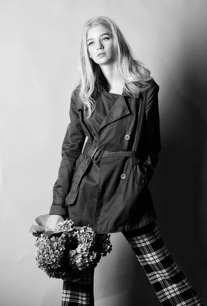 Must have concept. Woman blonde hair posing coat with flowers bouquet. Clothes and accessory. Girl fashion model wear coat for spring and autumn season. Trench coat fashion trend. Fashionable coat