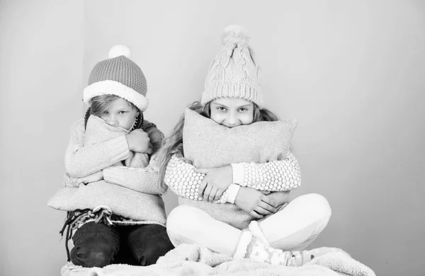 Siblings wear winter warm hats sit on pink background. Children boy and girl warm up with pillows and hats. Stay warm and comfortable. Warm up your winter wear with cute and cozy accessories