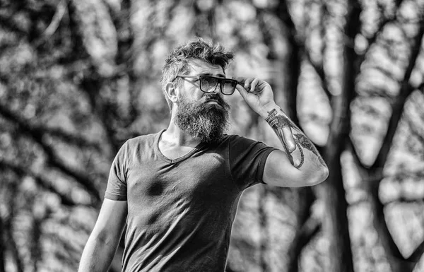 Man bearded with sunglasses nature background. Hipster confident in dark sunglasses. UV filter. Bearded hipster brutal man wear protective sunglasses. Bearded man wear modern fashionable sunglasses