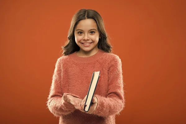 Girl hold book ler história sobre fundo laranja. Criança gosta de ler livro. Conceito de livraria. Maravilhosos livros infantis gratuitos disponíveis para ler. Literatura infantil. Atividades de leitura para crianças — Fotografia de Stock