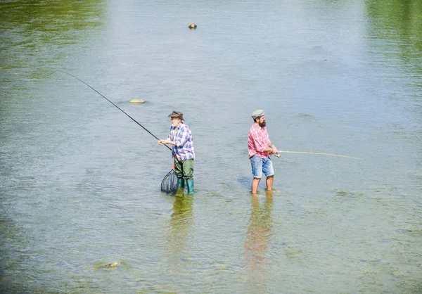 Hobby und sportliche Betätigung. Gemeinsam angeln. Männer stehen im Wasser. Angeln ist viel mehr als Fisch. Männerfreundschaft. Vater und Sohn angeln. Sommerwochenende. glücklicher Fischer mit Angel und Netz — Stockfoto