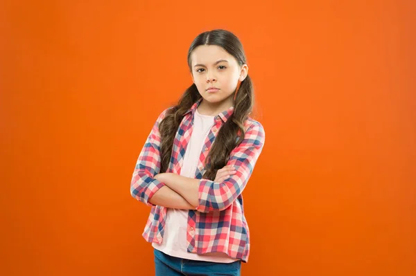 Estar chateado. memória da infância. menina laranja fundo. moda infantil. menina da escola séria. uniforme de trabalhador. Cabelo comprido. menina pequena camisa xadrez. Uma criança triste. dia das crianças — Fotografia de Stock