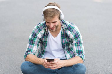 Çevrimiçi eğitim. Adam dışarıda sohbet ediyor. Adam yere oturur. Kulaklık takmış bir öğrenci. Boş zaman. Online eğitim. Müziği dinle. Kitap konsepti. Erkek kareli gömlek. Erkek modası. Öğrenci rahatlama telefonu kullan