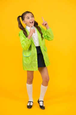 Gökyüzüne bak. Küçük bir okul çocuğu sarı arka planda parmağını gösteriyor. Moda yaylası giyen küçük çocuk. Sevimli küçük çocuk yağmurlu gün aktiviteleri zevk. Mutlu küçük kız okula geri