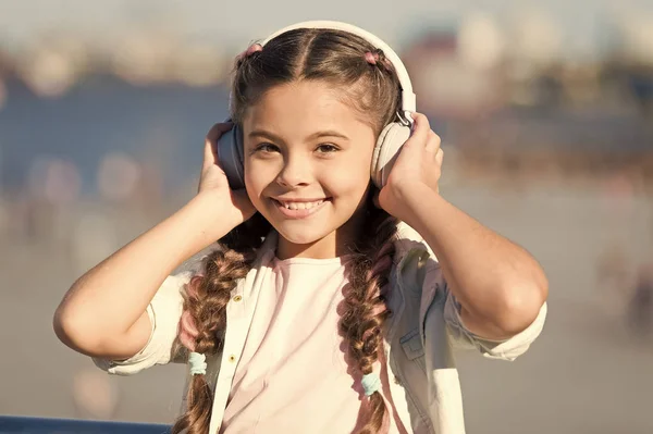 Seguire il flusso. Adorabile utente auricolare. Bambino piccolo con auricolare bianco regolabile. Ragazzina che usa cuffie bluetooth wireless all'aperto. Ragazzo carino che ascolta musica in cuffia stereo — Foto Stock