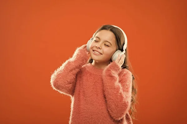 Niña linda niña usar auriculares escuchar música. Niño escuchar música fondo naranja. Música recomendada basada en el interés inicial. Las mejores aplicaciones de música gratis para tu dispositivo móvil. Disfruta del sonido — Foto de Stock