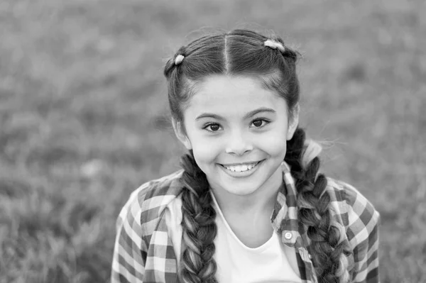 Sorriso encantador. Menina pequena criança com penteado de tranças na moda. Tendência moda. Salão e cuidados com o cabelo. Menina sorrir rosto ao ar livre. Caminhada agradável no parque. Sorriso e alegria. Penteado na moda para crianças — Fotografia de Stock