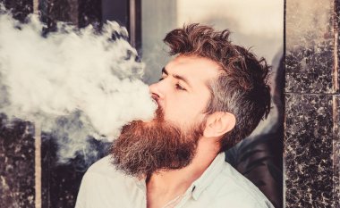 Elektronik sigara içiyor. Stres giderme konsepti. Sigara içme cihazı. Adam uzun sakal sigara alışkanlığı ile rahat. Aromalı duman bulutları. Sakallı adam vape içiyor. Sakallı adam duman solumak