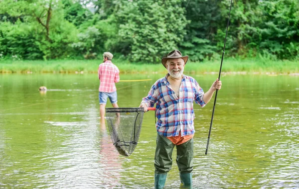 Activity and hobby. Fishing freshwater lake pond river. Bearded men catching fish. Mature man with friend fishing. Summer vacation. Happy cheerful people. Master baiter. Fisherman with fishing rod