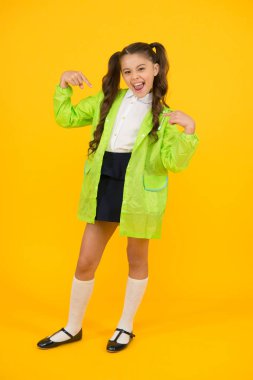 Ben iyiyim. Mutlu küçük çocuk sarı arka plan üzerinde parmaklarını işaret. Sonbahar günü küçük bir okul çocuğu. Küçük kız yağmurlu havalarda okula dönüyor. Yeşil raingear sevimli küçük çocuk