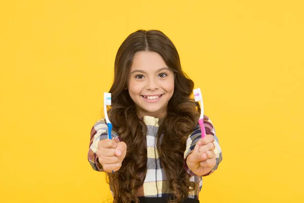 Двічі швидше. Дівчина мила довге волосся тримає зубні щітки жовтим тлом. Дитяча дівчинка тримає дві зубні щітки. Дитяча школярка розумна дитина щасливе обличчя піклується про гігієну. Концепція зубів пензлем. Гігієна зубів — стокове фото