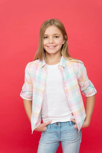 In ihrem eigenen Stil. modisches kleines Mädchen. Kindermode. stilvolle Schönheit. kleines Mädchen roter Hintergrund. glückliche Kindheit. Lächelndes blondes Kind. Mädchen mit langen blonden Haaren. Casual Style. Kindertag — Stockfoto