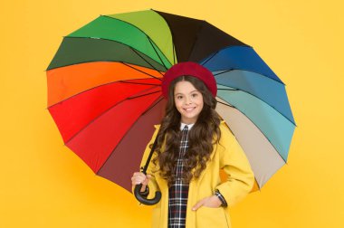 Yağmurlu gün eğlencesi. Şemsiye altında iyi yürüyüşler. Yağmur konseptinin tadını çıkar Çocuk mutlu bir şekilde renkli gökkuşağı şemsiyesi tutuyor. Yağmurlu hava ve uygun giysiler. Parlak şemsiye. Eğlenmene bak. Pozitif olma kavramı