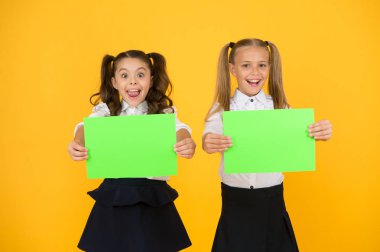 Okul için reklam fikri. Mutlu kızlar sarı arka plan üzerinde belirli bir fikir için kağıt çarşaf tutan. Küçük sevimli çocuklar dahice fikir gülümsüyor. Fikriniz için boş kağıt ile küçük çocuklar, kopya alanı