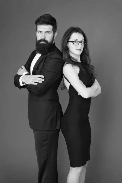 Formal fashion and elegant clothes. Luxury fashion boutique. Fashion clothes shop. Official event. Couple man in tuxedo and elegant girl. Man bearded hipster and woman in formal dress red background