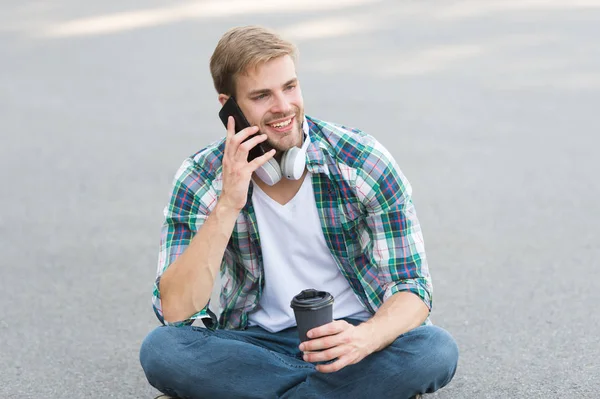 Call friend. Wellbeing and health. Having coffee break. Man sit on ground while drinking coffee. Relax and recharge. Have fun during break. Guy carefree student enjoy coffee outdoors. Life balance