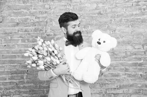 Romantic man with flowers and teddy bear. Romantic gift. Macho getting ready romantic date. Man wear blue tuxedo bow tie hold flowers bouquet. International womens day. Surprise will melt her heart