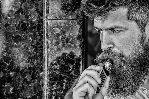 Бородатый человек курит вапе. Человек с бородой выдыхает дым. Курение электронных сигарет. Концепция снятия стресса. Курящее устройство. Мужчина с длинной бородой, расслабленный от курения. Облака ароматного дыма