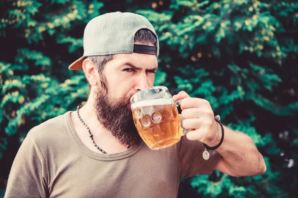 Hipster homem barbudo brutal segurar caneca cerveja fresca fria. A cerveja artesanal é jovem, urbana e elegante. Conceito de cerveja e cerveja. Homem relaxante desfrutando de cerveja quente dia de verão. Saciar a sede. Bebida alcoólica e bar — Fotografia de Stock