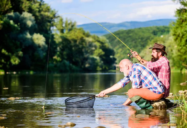 Les amis passent du bon temps au bord de la rivière. Belle soirée bord de rivière. Pêcheur expérimenté montrer des conseils à son fils. Transfert des connaissances. Les hommes pêchent le poisson au bord de la rivière. Enseigner la pêche. Partager ses secrets — Photo