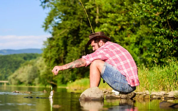 Hombre barbudo maduro con pescado en caña. pesca de caza mayor. relajarse en la naturaleza. pasatiempo peces mosca. Actividad de verano. pescador exitoso en el agua del lago. pesca hipster con cuchara-cebo. Pesca de caza mayor —  Fotos de Stock