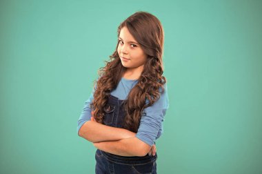 Çocuk el ele tutuşup göğsünü sıkıca bağladı. Çocuk psikolojisi ve gelişimi. Kendine güvenen duruş. Yetiştirme güveni Uzun saçlı, kendine güvenen bir çocuk. Kıvırcık saçlı kız kendine güveniyor.