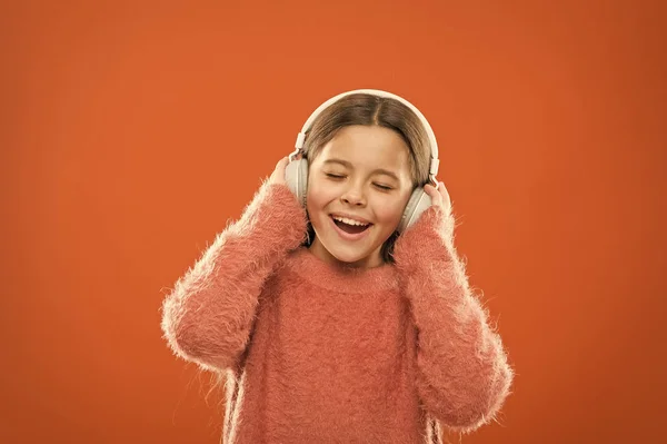 Disfruta del sonido. Niña linda niña usar auriculares escuchar música. Niño escuchar música fondo naranja. Música recomendada basada en el interés inicial. Las mejores aplicaciones de música gratis para tu dispositivo móvil — Foto de Stock