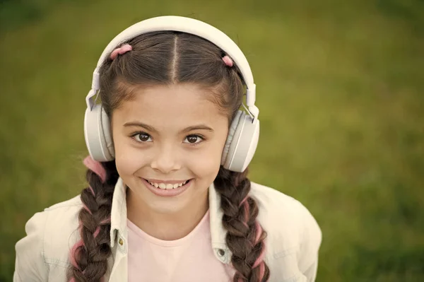 Escucha música mientras te relajas al aire libre. Niña disfrutar de la música mientras se sienta en el prado de hierba verde. Tiempo libre agradable. Los auriculares infantiles escuchan música. Moda chica bastante cool en los auriculares escuchando música — Foto de Stock