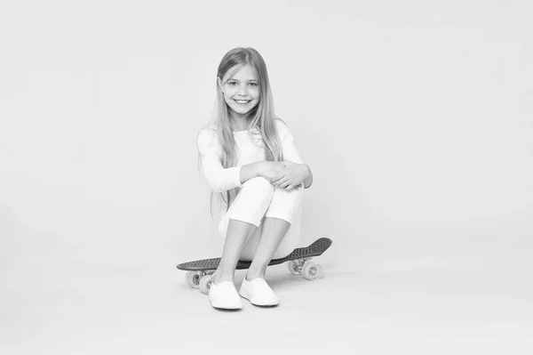 Chica divirtiéndose con penny board fondo rosa. Niño adorable niño pelo largo adoro paseo penny board. Montar tablero de peniques y hacer trucos. A la chica le gusta andar en monopatín. El ocio activo de la muchacha de moda — Foto de Stock