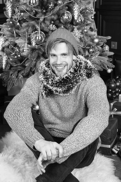 남자가 미소 모자, 스웨터, 크리스마스 나무에 틴 셀 — 스톡 사진