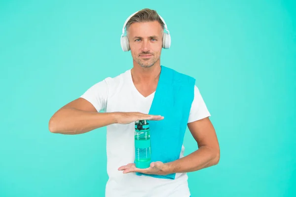 Beber agua es clave para alcanzar los objetivos de fitness. Hábitos saludables para beber. Un hombre guapo con auriculares sostiene una botella de agua potable. Agua potable para una mejor deshidratación. Presentación y publicidad — Foto de Stock