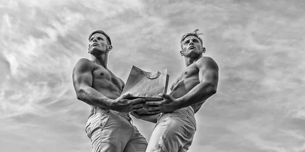 Brothers buy eco healthy products. Guys attractive twins carry shopping bag made out of brown paper. Sales season. Men muscular athletes hold shopping bag sky background. Hot sales and discount — Stock Photo, Image