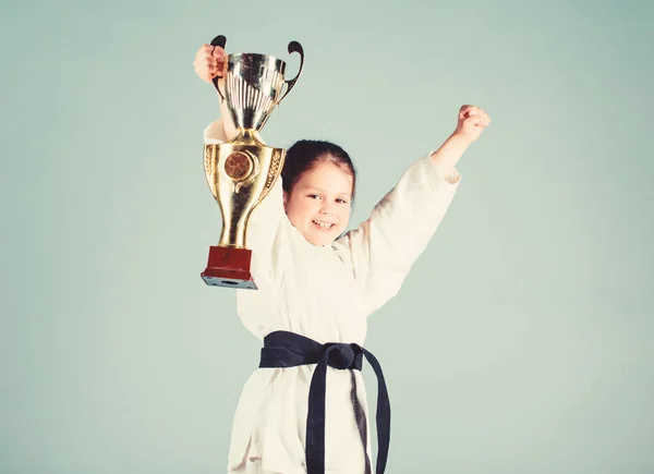 small girl with champion cup. martial arts. winner little girl in gi sportswear. practicing Kung Fu. childhood. knockout. energy and activity for kids. sport success in single combat. Sporty beauty