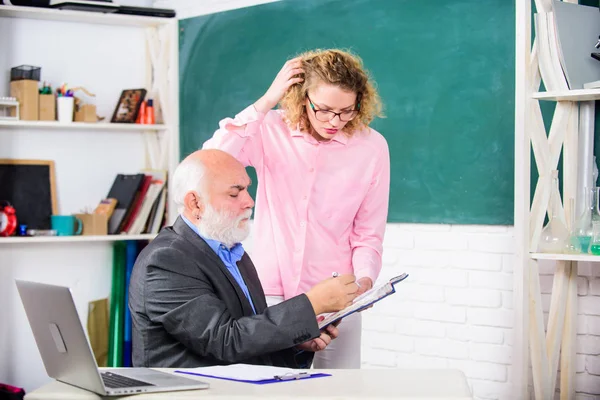 Student asking teacher about task. Solving math tasks. School education concept. Check homework. Educator and student looking at book. Explaining difficult topic. Student puzzled by some information