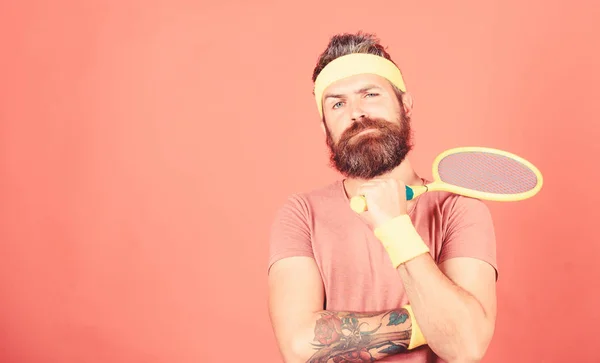 Tennis sport and entertainment. Concentrated on tennis court. Athlete hipster hold tennis racket in hand red background. Man bearded hipster wear sport outfit. Tennis player beginner retro fashion