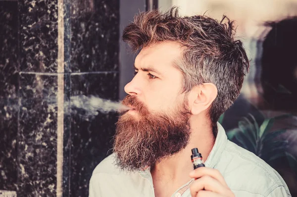 Un brutal macho barbudo fumando cigarrillo electrónico. Hipster maduro con barba. hipster hombre mantenga el dispositivo de vapeo. Hombre fumando ecigarette. Seguridad y adicción a la salud. inhalando vapor. Encendido de cigarrillos — Foto de Stock