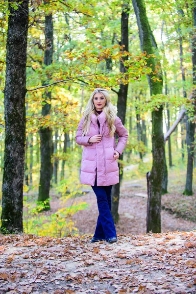 Girl fashionable blonde walk in autumn forest. Woman wear warm pink jacket. Jackets everyone should have. Best puffer coats to buy. How to rock puffer jacket like a star. Puffer fashion concept — Stock Photo, Image