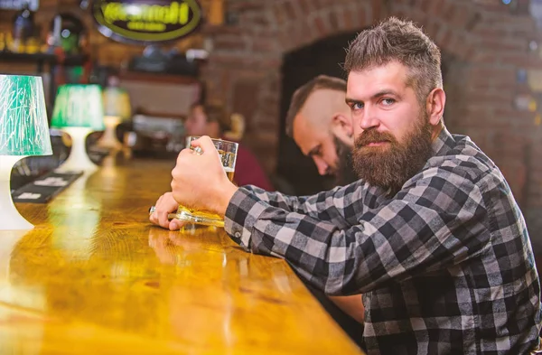 Homem barbudo hipster brutal senta-se no balcão do bar a beber cerveja. Peça bebida alcoólica. O bar é um lugar relaxante, tome uma bebida e relaxe. Hipster relaxando no bar com cerveja. Homem com barba passar o lazer no bar escuro — Fotografia de Stock