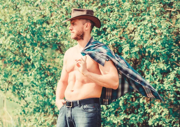 Strong and confident cowboy. Owner of rancho. Man unshaven face muscular torso cowboy. Farm concept. Guy bearded cowboy in nature. Macho six packs torso wear rustic style clothes and cowboy hat