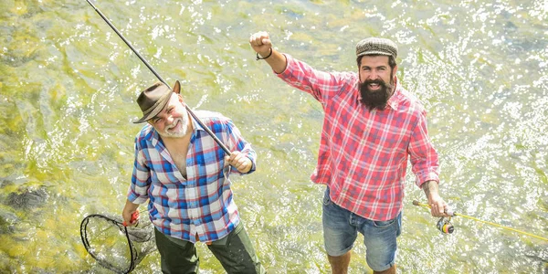 Padre e hijo pescando. pasatiempo y actividad deportiva. Cebo para truchas. fin de semana de verano. hombres maduros pescador. amistad masculina. vinculación familiar. dos pescador feliz con caña de pescar y red. inteligencia colectiva — Foto de Stock