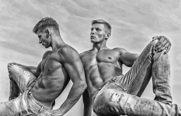 牛仔长裤强调男性性行为。男子双胞胎兄弟肌肉男坐在放松天空背景。男性强壮的肌肉运动员健美放松。神圣之美。性感躯干迷人的身体 — 图库照片