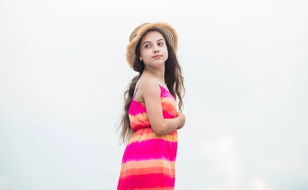 hat fits perfect. cloudy weather. happy childrens day. carefree child in summer dress. small girl with long curly hair. childhood happiness. summer kid fashion. small girl spend time outdoor