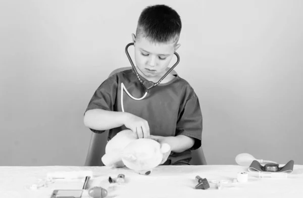 El pequeño doctor está ocupado sentándose en la mesa con herramientas médicas. Examen médico. Concepto de medicina. Procedimientos médicos para el oso de peluche. Niño lindo niño futuro médico carrera. Trabajador del hospital. Asistencia sanitaria —  Fotos de Stock