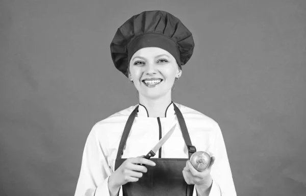 Dania kuchni. Kobieta w kapeluszu kucharza i Apron. Szczęśliwa kobieta gotowanie zdrowej żywności przez przepis. Gospodyni domowa z nożem do gotowania i cebulą. profesjonalnego kucharza w kuchni. Bycie głodnym — Zdjęcie stockowe