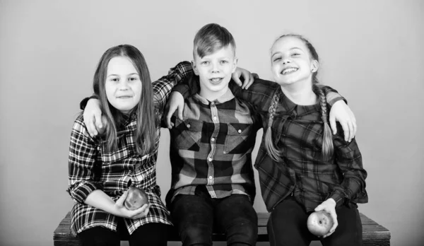 Boy and girls friends in similar checkered clothes eat apple. Teens with healthy snack. Healthy dieting and vitamin nutrition. Eat fruit and be healthy. Friends kids hug each other. Healthy lifestyle