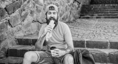 Adam sakallı hızlı atıştırmalık ve içecek kağıt fincan zevk. Sokak Yemekleri çok güzel. Kentsel yaşam tarzı beslenme. Merdivenlerde oturup Carefree hipster önemsiz yiyecek yemek. Aç adam atıştırmalığı. Önemsiz yiyecekler. Adam yemek sıcak köpek