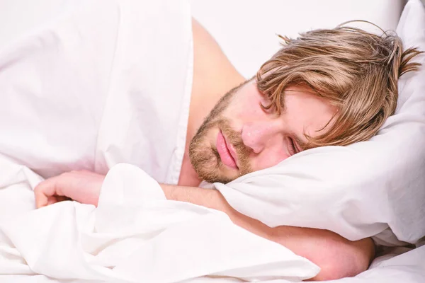 Afbeelding van de jonge man die zich uitstrekt in bed. Close-up van voeten in een bed onder witte deken. Man voelt moe en wil niet opstaan. — Stockfoto