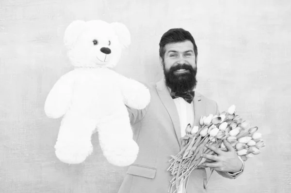 Surprise for her. Gentleman making romantic surprise for her. Gentleman romantic gift. Birthday greetings. Happy birthday my love. Man bearded gentleman suit bow tie hold teddy bear and bouquet — Stock Photo, Image